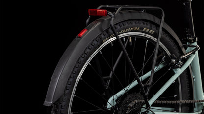 Nahaufnahme des Hinterrads des CUBE Ella 240 aloegreen'n'white 2025 mit Schwalbe-Reifen, Shimano 3x8-Schaltung, schwarzem Schutzblech, Gepäckträger und rotem Reflektor vor schwarzem Hintergrund.