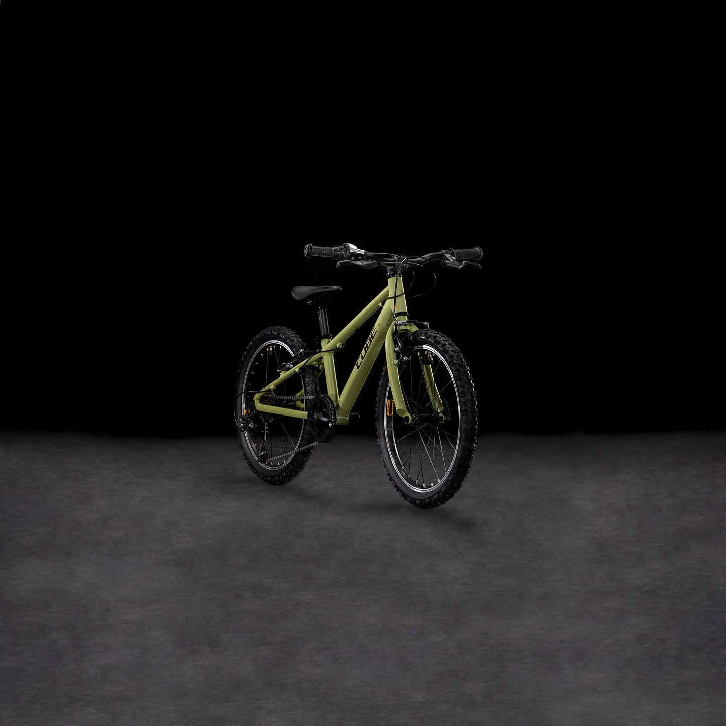 Ein CUBE Acid 200 lightolive'n'orange 2025 Kinder-Mountainbike mit schwarzen Rädern, Lenker und V-Bremsen steht auf einer dunkel strukturierten Oberfläche vor einem schwarzen Hintergrund.