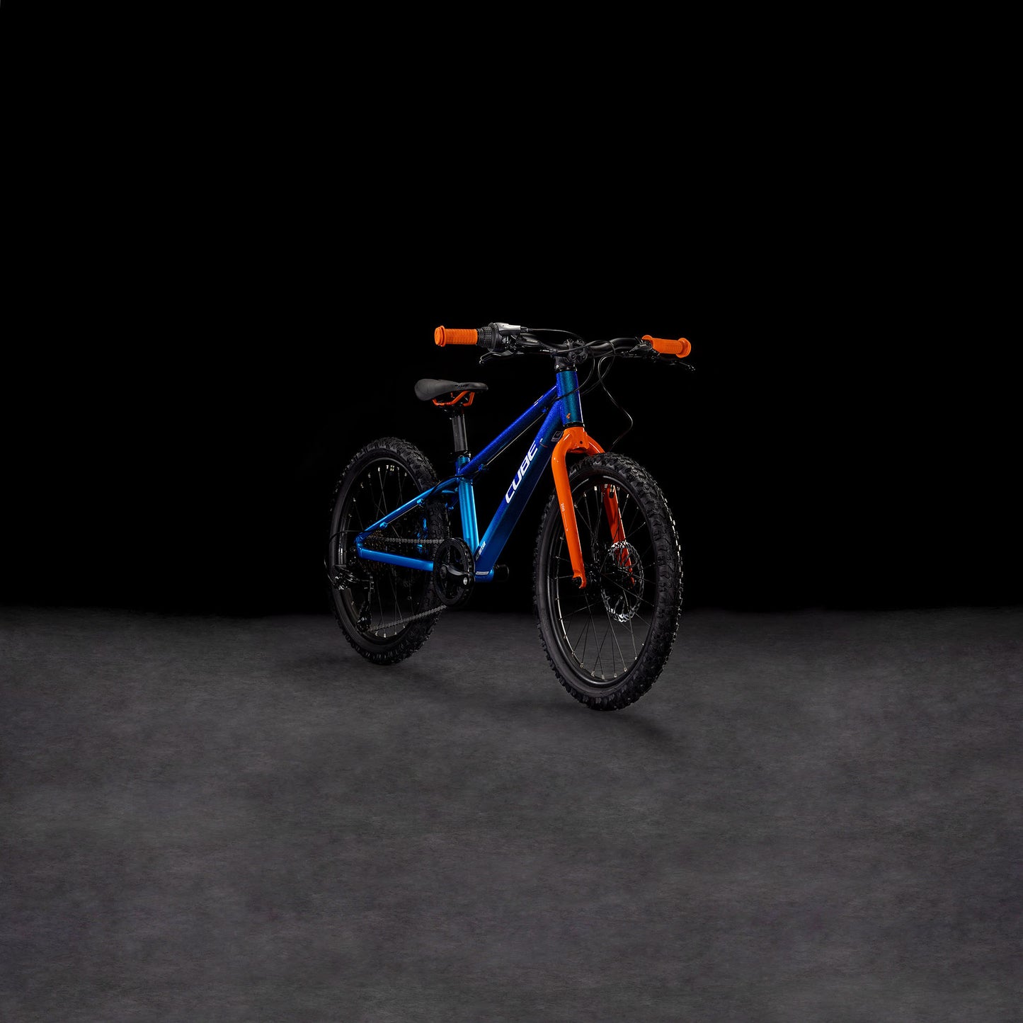 Auf einer dunklen, glatten Fläche vor schwarzem Hintergrund ist das CUBE Acid 200 Disc actionteam 2025 Kinder-Mountainbike in Blau und Orange mit hydraulischen Scheibenbremsen abgebildet.