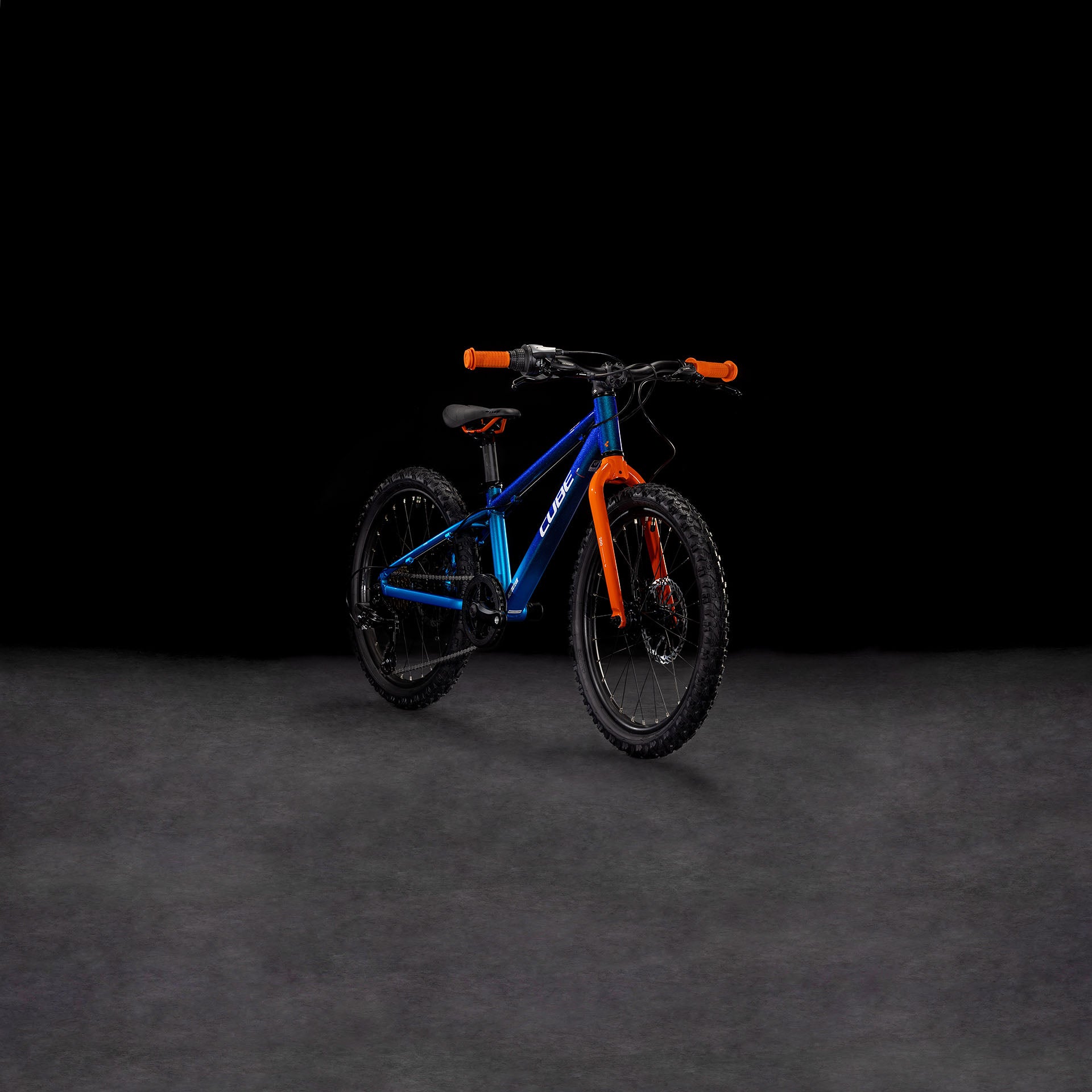 Auf einer dunklen, glatten Fläche vor schwarzem Hintergrund ist das CUBE Acid 200 Disc actionteam 2025 Kinder-Mountainbike in Blau und Orange mit hydraulischen Scheibenbremsen abgebildet.