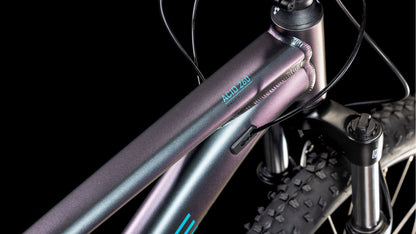 Nahaufnahme des CUBE Acid 260 Disc galactic'n'cyan 2025 Mountainbike-Rahmens mit detaillierten Schweißnähten, Shimano-Schaltung, Federgabel, Reifenprofil und schwarzen Kabeln auf einem Aluminiumrahmen - alles vor einem schwarzen Hintergrund.