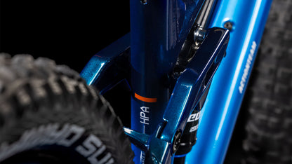 Nahaufnahme des blauen Cube Stereo 240 ONE actionteam 2025 von CUBE mit der Hinterradaufhängung, dem Reifenprofil und dem HPA-Label. Der detaillierte Rahmen und die robusten Komponenten heben sich von einem dunklen Hintergrund ab.
