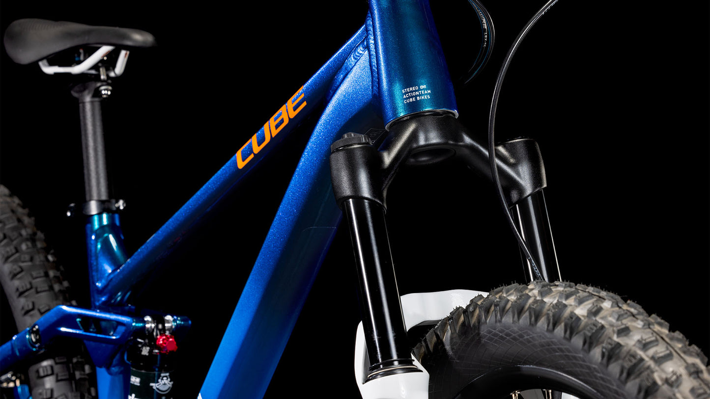 Nahaufnahme eines blauen CUBE Stereo 240 ONE actionteam 2025 Kinder-Mountainbikes, die die vordere Federgabel, den dicken Vorderreifen, den Teilrahmen und den Sattel vor einem schwarzen Hintergrund zeigt.