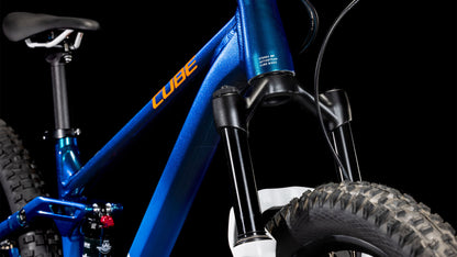 Nahaufnahme eines blauen CUBE Stereo 240 ONE actionteam 2025 Kinder-Mountainbikes, die die vordere Federgabel, den dicken Vorderreifen, den Teilrahmen und den Sattel vor einem schwarzen Hintergrund zeigt.