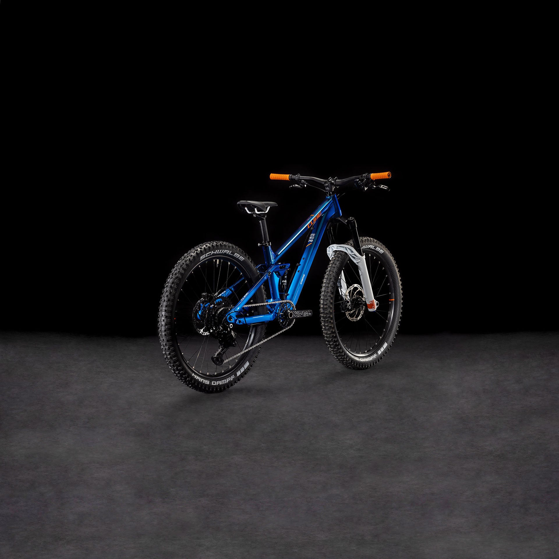 Das CUBE Stereo 240 ONE actionteam 2025, ein 24-Zoll-Mountainbike für Kinder mit dicken Reifen, orangefarbenen Lenkergriffen und einer silbernen Federgabel, ist vor einem dunklen Hintergrund abgebildet.