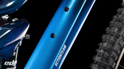 Nahaufnahme des blauen Cube Stereo ONE22 Rookie actionteam Rahmens von CUBE mit aufgedrucktem ACTIONTEAM, zwei Befestigungsschrauben und einem Noppen-Hinterreifen vor schwarzem Hintergrund. Shimano 11-fach Schaltung steigert die Leistung.
