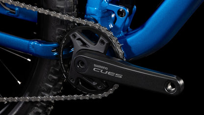Nahaufnahme einer CUBE-Kurbelgarnitur und -Kette auf einem blauen Cube Stereo ONE22 Rookie actionteam-Rahmen. Hervorgehoben sind das Kettenblatt, der Kurbelarm und ein Teil des Hinterradreifens mit einer 11-fach Shimano-Schaltung vor einem schwarzen Hintergrund.