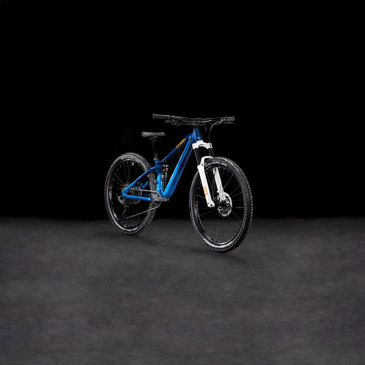 Das Cube Stereo ONE22 Rookie actionteam von CUBE, mit dicken Reifen und einer Shimano 11-fach Schaltung, ist in blau und weiß auf einem schlichten dunklen Hintergrund abgebildet, leicht nach links geneigt.