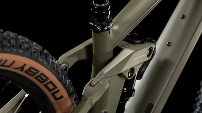 Nahaufnahme der Hinterradaufhängung des CUBE Stereo ONE44 HPC Rookie dustyolive'n'gold 2025, die den Carbonrahmen, den Dämpfer und den Schwalbe Nobby Nic-Reifen mit hellbrauner Seitenwand vor schwarzem Hintergrund zeigt.
