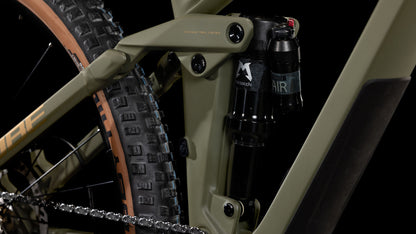 Nahaufnahme der Hinterradaufhängung des CUBE Stereo ONE44 HPC Rookie dustyolive'n'gold 2025, die den Stoßdämpfer, den Schwalbe Nobby Nic-Hinterradreifen und einen Teil des olivgrünen Carbonrahmens vor einem schwarzen Hintergrund zeigt.