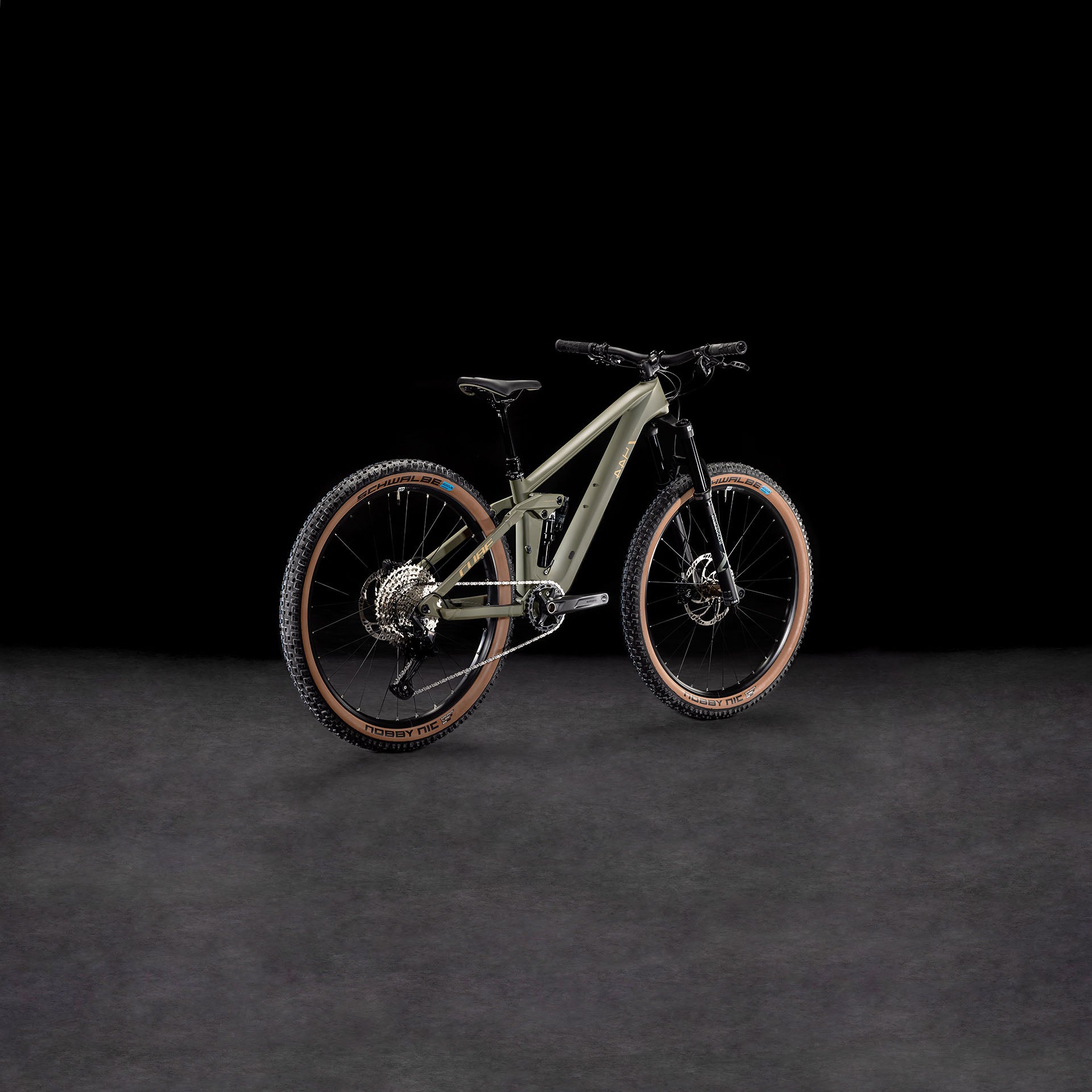 Das CUBE Stereo ONE44 HPC Rookie dustyolive'n'gold 2025 ist ein modernes Mountainbike mit mattem, olivgrünem Carbonrahmen, braunen Schwalbe Nobby Nic-Reifen, Vorderradfederung und robustem Offroad-Design, das sich vor einem dunklen Hintergrund präsentiert.