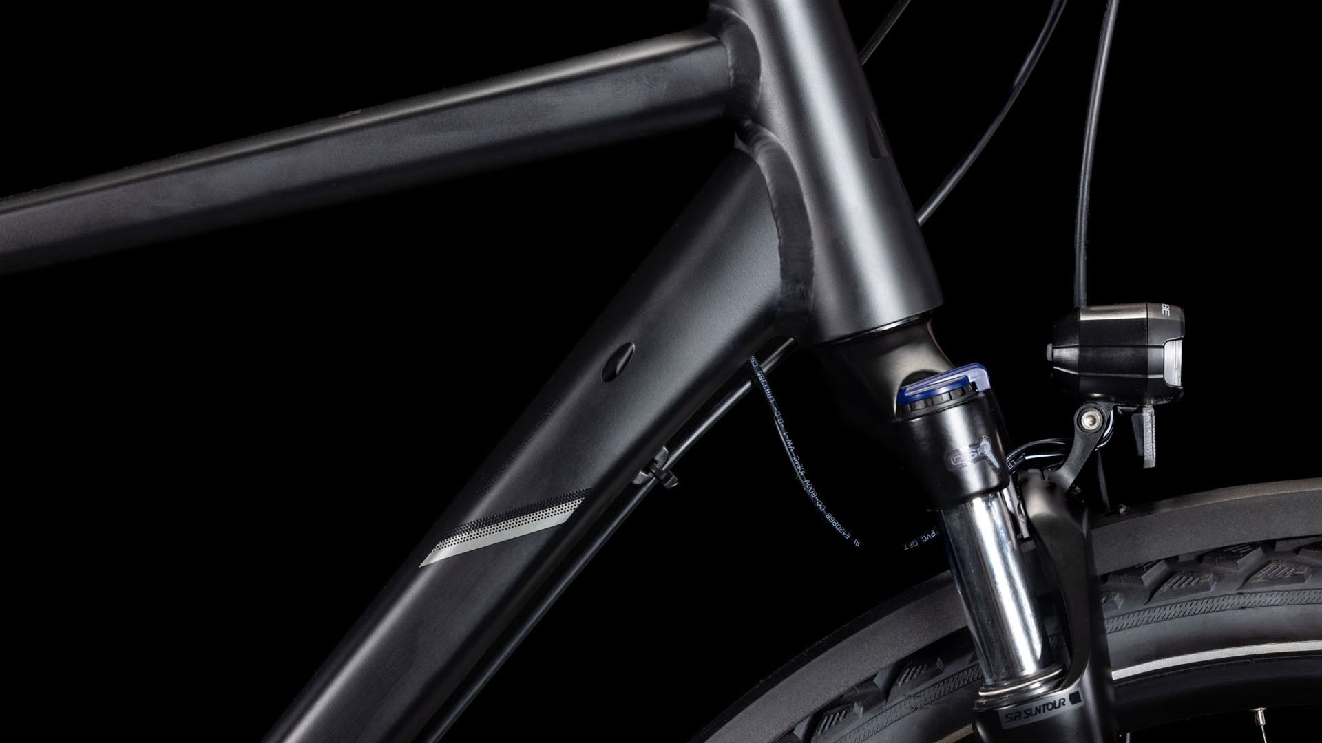 Nahaufnahme des CUBE Nature ONE Allroad black'n'black Rahmens und der Federgabel, mit einem Teil des Vorderrads und einem Scheinwerfer vor einem schwarzen Hintergrund.