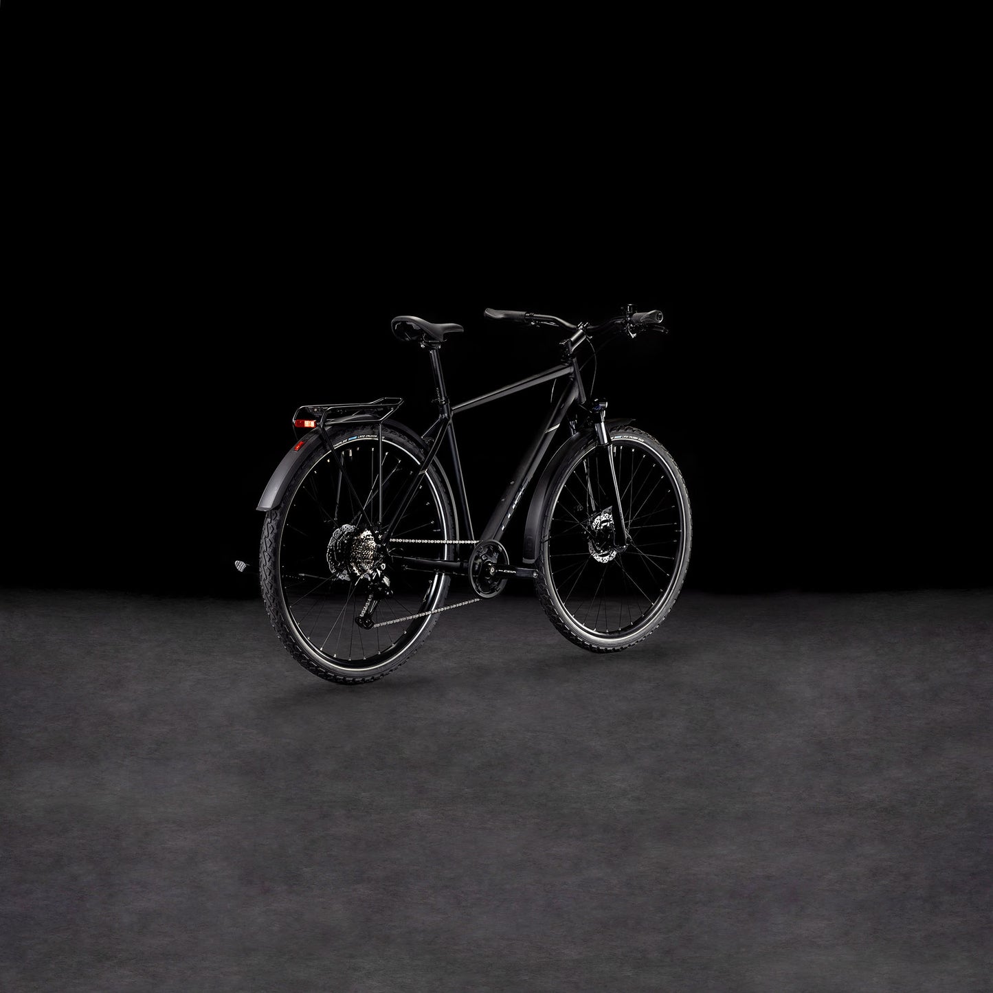 Ein schnittiges CUBE Nature ONE Allroad black'n'black Fahrrad mit Gepäckträger und Schutzblechen steht auf einer nebligen, dunklen Fläche vor einem schwarzen Hintergrund. Sein modernes Design wird schräg hervorgehoben und die hydraulischen Scheibenbremsen sorgen für zuverlässige Bremskraft.