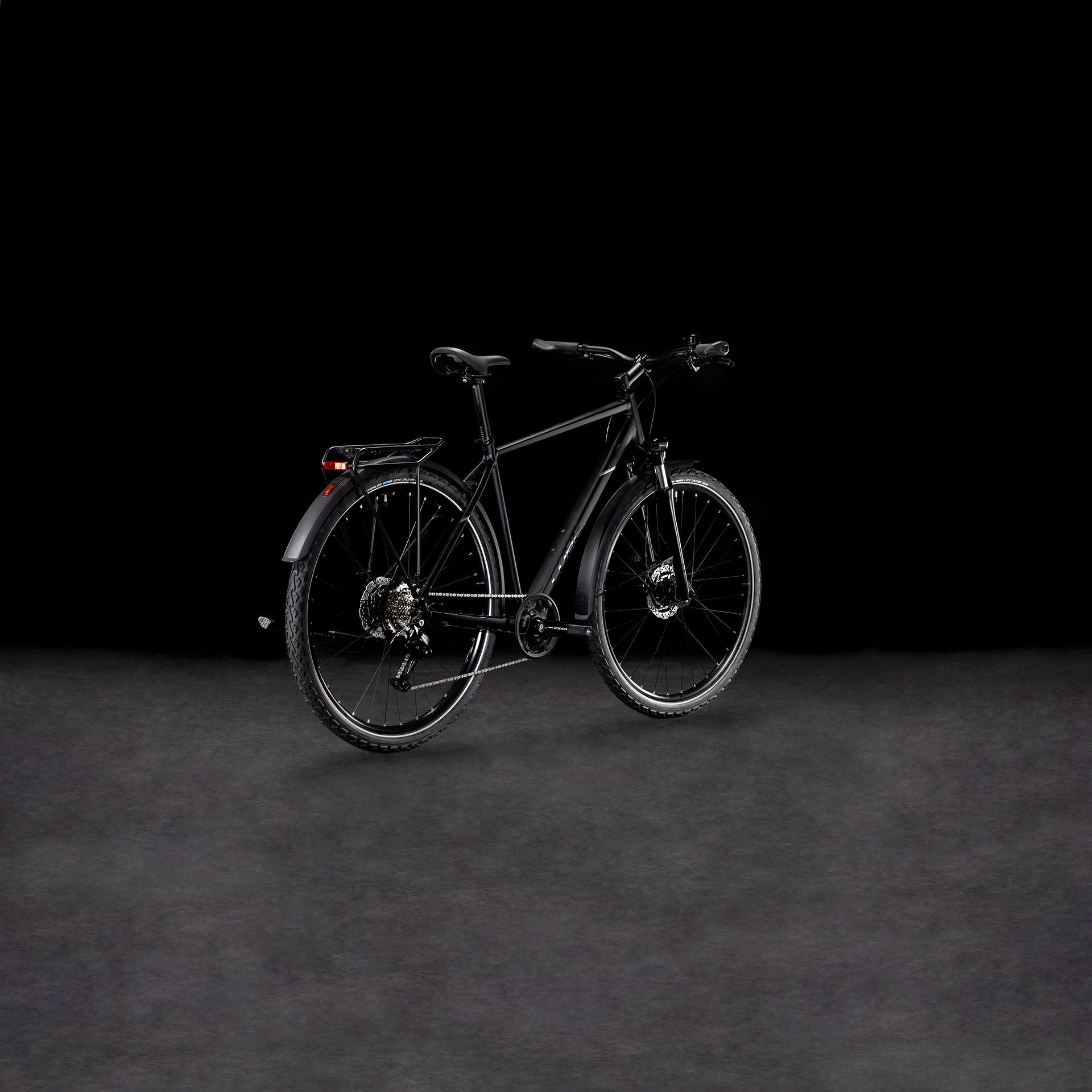 Ein schnittiges CUBE Nature ONE Allroad black'n'black Fahrrad mit Gepäckträger und Schutzblechen steht auf einer nebligen, dunklen Fläche vor einem schwarzen Hintergrund. Sein modernes Design wird schräg hervorgehoben und die hydraulischen Scheibenbremsen sorgen für zuverlässige Bremskraft.