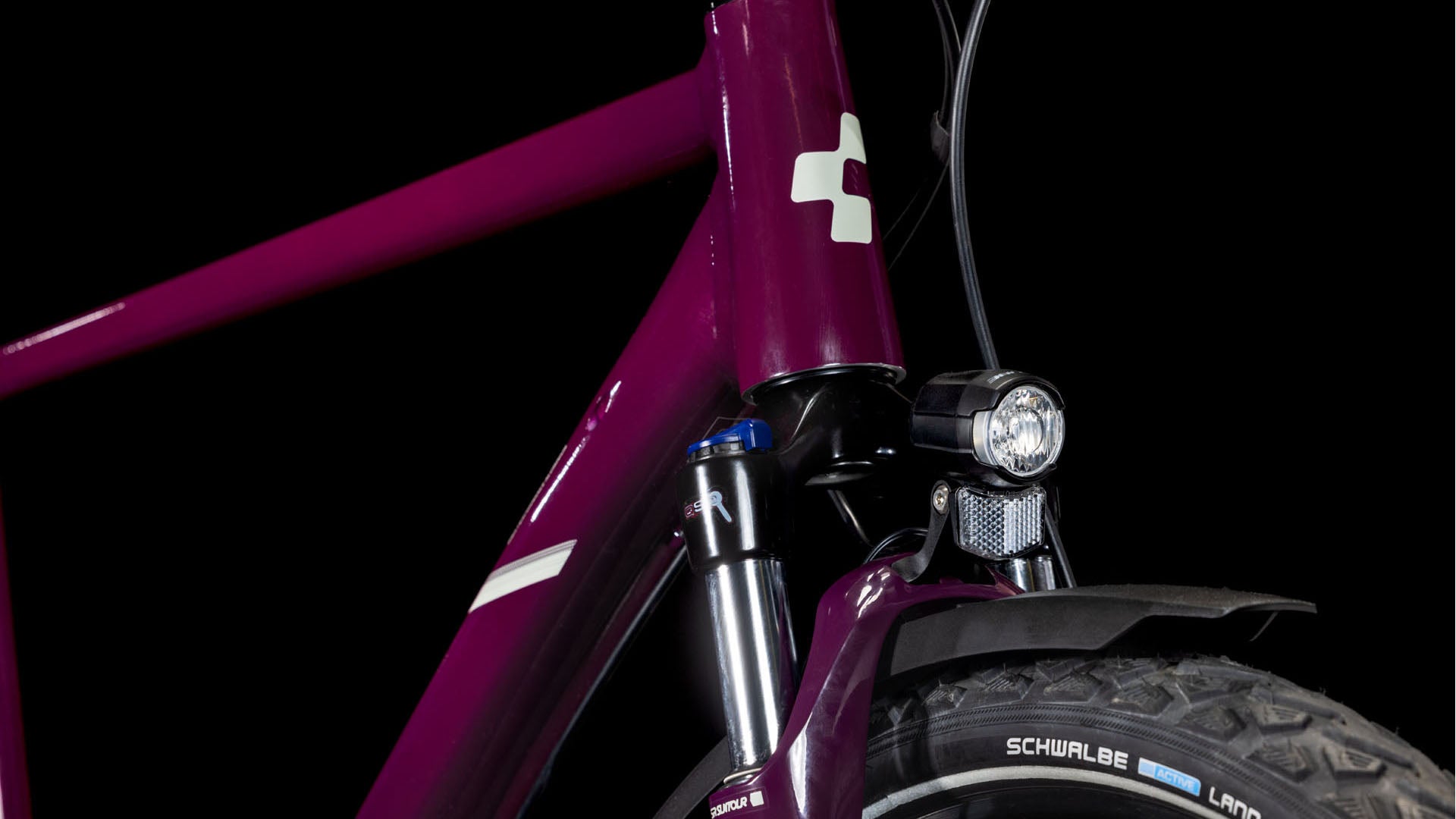 Nahaufnahme der Frontpartie des CUBE Nature ONE Allroad amarone'n'lunar 2025, die den Rahmen, die Shimano 1x8-Gang-Schaltung, die Federgabel, den Scheinwerfer, das Schutzblech und den Schwalbe-Reifen vor einem schwarzen Hintergrund zeigt.