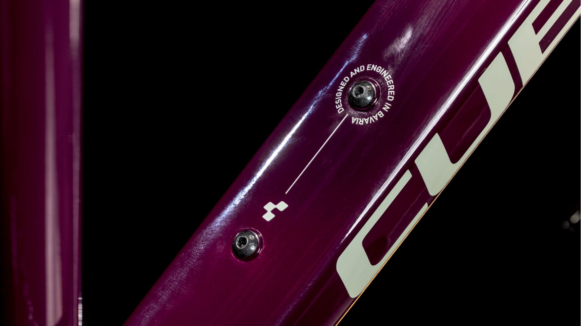 Nahaufnahme des CUBE Nature ONE Allroad amarone'n'lunar Trapeze 2025 Trekkingrad-Rahmens mit einer Schraube, einem Schild mit der Aufschrift DESIGNED AND ENGINEERED IN GERMANY, einem Teil des CUBE-Logos und Details der Shimano 1x8-Gang Schaltung.