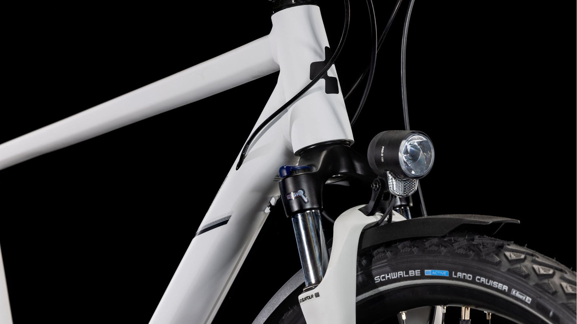 Nahaufnahme der Vorderseite des CUBE Nature Pro Allroad cotton'n'grey 2025, die den Aluminiumrahmen, das Steuerrohr, die vordere Federgabel, den montierten Scheinwerfer und den Schwalbe Land Cruiser-Reifen vor einem schwarzen Hintergrund zeigt.