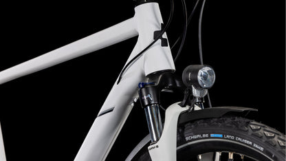 Nahaufnahme der Vorderseite des CUBE Nature Pro Allroad cotton'n'grey 2025, die den Aluminiumrahmen, das Steuerrohr, die vordere Federgabel, den montierten Scheinwerfer und den Schwalbe Land Cruiser-Reifen vor einem schwarzen Hintergrund zeigt.