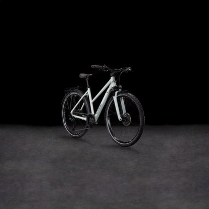 Das CUBE Nature EXC Allroad seasalt'n'pyrite Trapeze, ein weißes Durchstiegs-E-Bike mit schwarzen Reifen und Lenker und Shimano Cues 2x11-Gang Schaltung, wird auf einer dunkel strukturierten Oberfläche vor einem schwarzen Hintergrund präsentiert.