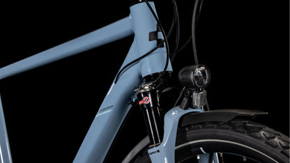 Nahaufnahme des vorderen Rahmens des CUBE Nature EXC Allroad pigeonblue'n'black Fahrrads, mit Hervorhebung des Steuerrohrs, der vorderen Federgabel, des Scheinwerfers, der Kabel, der hydraulischen Scheibenbremsen und eines Teils des Vorderreifens vor einem schwarzen Hintergrund.