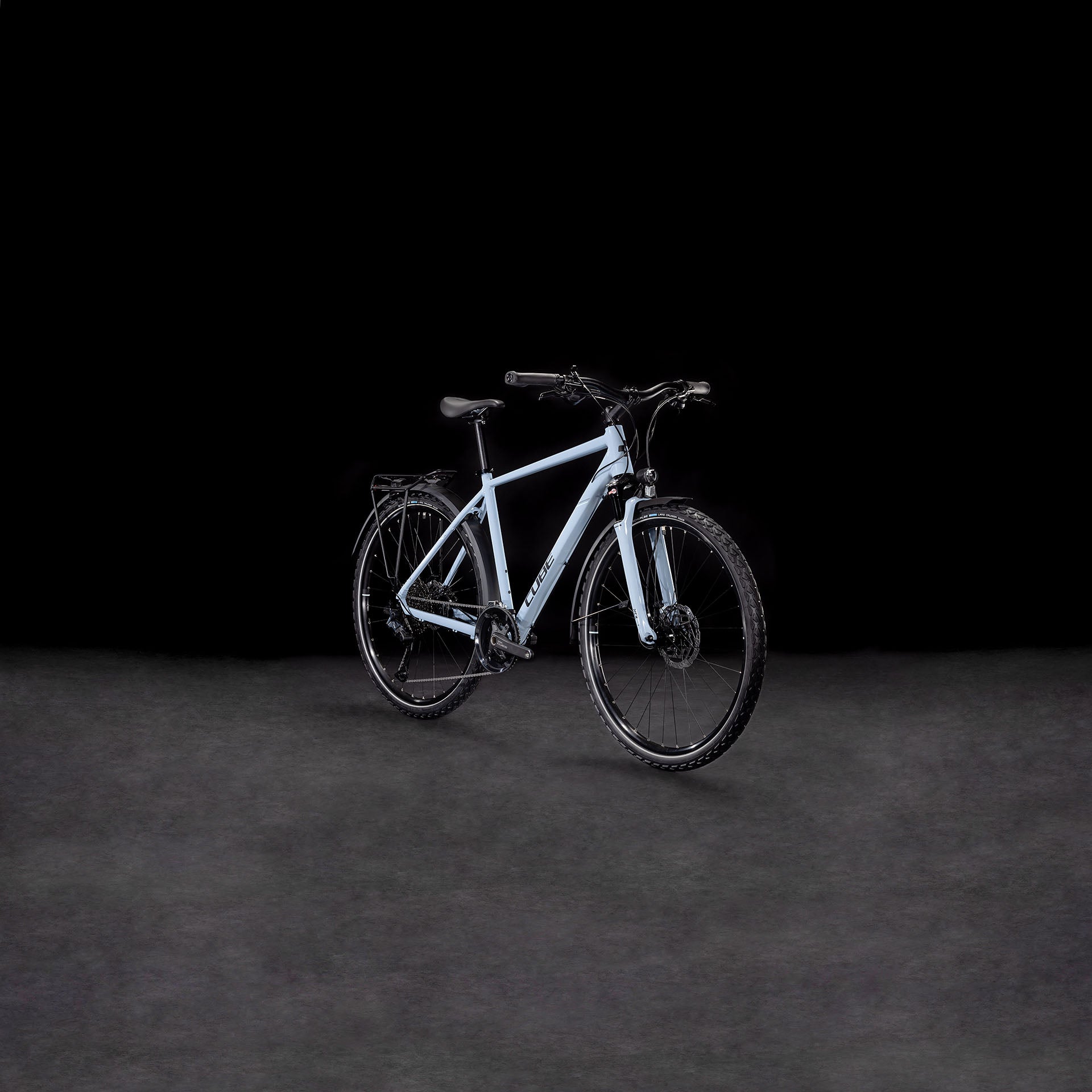 Das CUBE Nature EXC Allroad pigeonblue'n'black Elektrofahrrad mit schwarzen Reifen, Lenker und hydraulischen Scheibenbremsen ist in einem leichten Seitenwinkel auf einem dunklen, neutralen Hintergrund abgebildet.