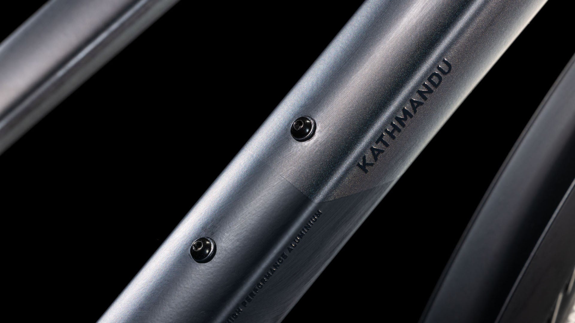 Nahaufnahme des Rahmenrohrs des Cube Kathmandu SLX nightsky'n'ink Trapeze 2025 von CUBE mit dem Schriftzug "KATHMANDU" und zwei Befestigungslöchern auf schwarzem Hintergrund - für umweltfreundliche Mobilität.