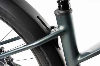 Nahaufnahme eines Fahrradrahmens mit Hinterrad und Sattelrohr in glatter Metallic-Optik, ausgestattet mit dem ACID Gepäckträger SIC 2.0 RAIL schwarz zur Befestigung von Packtaschen an der Rahmen- und Sattelstrebenverbindung.