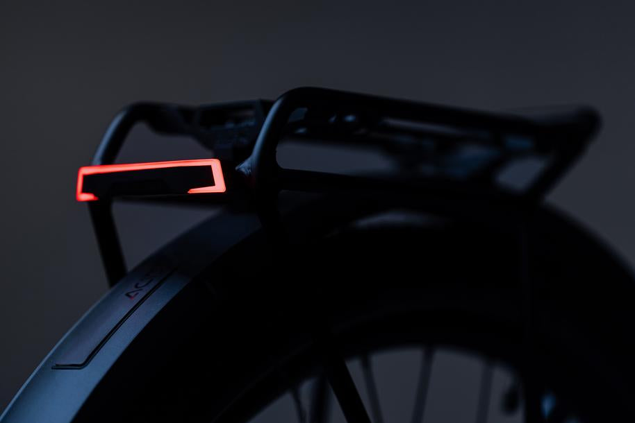 Nahaufnahme des Gepäckträgers und des Reifens eines Fahrrads mit dem ACID E-Bike Gepäckträgerrücklicht PRO-E HPP schwarz BES3 mit rotem LED-Licht, StVZO-geprüft, das die Dunkelheit um Bosch BES3-Motoren ausleuchtet.