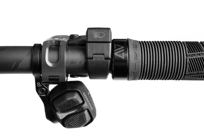 Nahaufnahme eines ACID E-Bike-Frontlichts PRO-E 200 High Beam X-Connect, strukturierter schwarzer Griff, Gangschaltung und X-Connect-Bedientasten an einem Fahrradlenker, alles vor einem weißen Hintergrund.