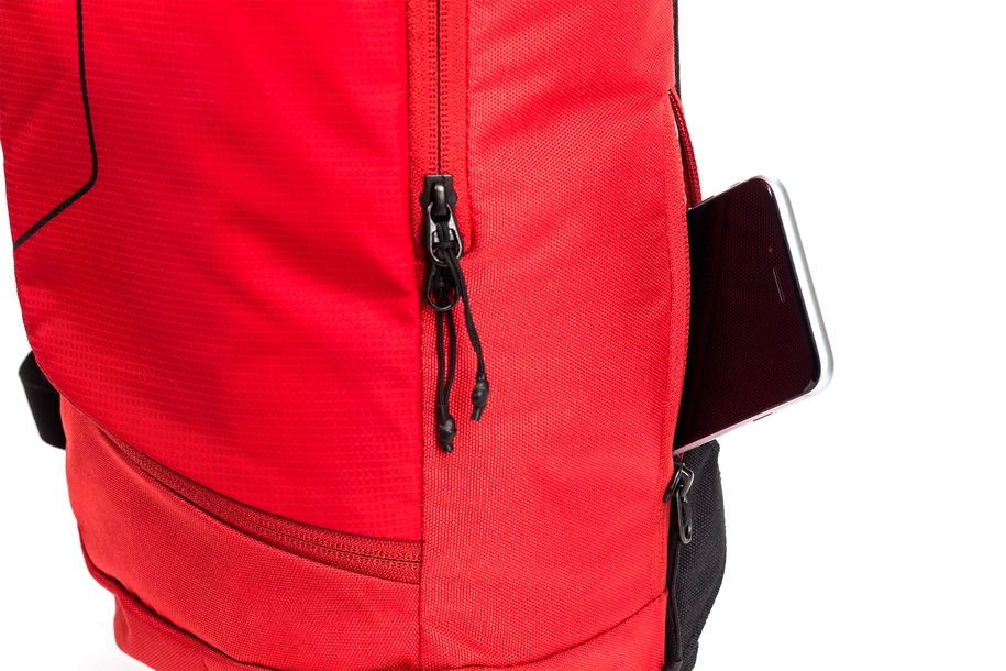 Ein schwarzes Smartphone lugt aus der Seitentasche eines leuchtend roten CUBE Rucksacks PURE TEN Red von Cube mit dem Natural Fit Rückensystem vor weißem Hintergrund hervor.