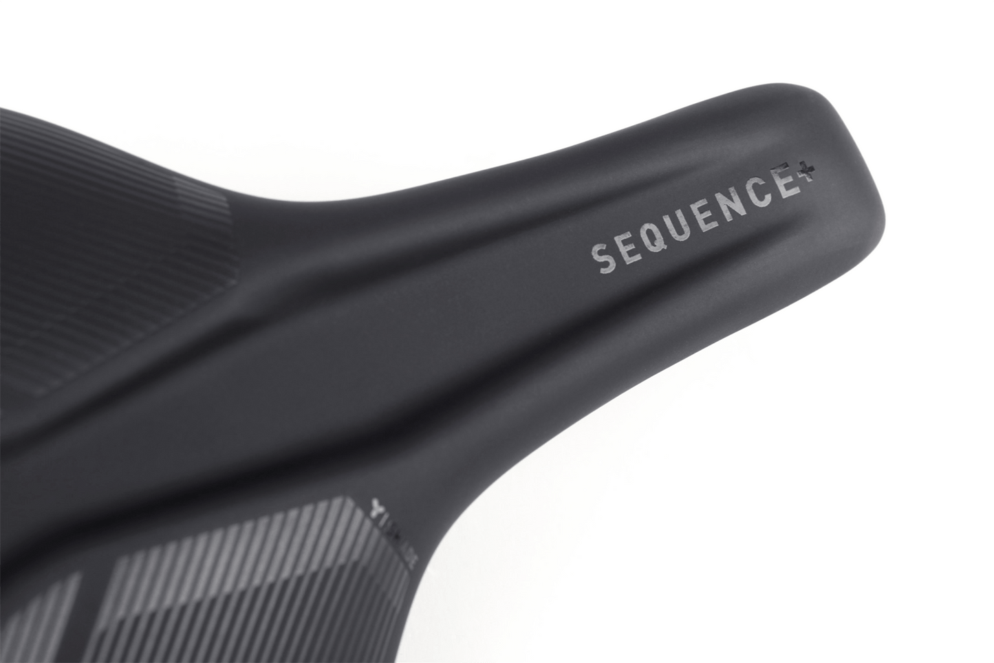 Nahaufnahme des Natural Fit Sattel Sequence+ Regular von Natural Fit, ein schwarzer Sattel mit SEQUENCE+ in weiß, mit Deep-Shell Sattelschale und einer strukturierten Oberfläche für verbesserten Komfort und modernen Stil.