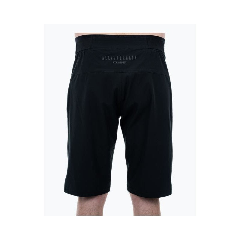 Eine Person trägt eine schwarze CUBE ATX Baggy Shorts CMPT inkl. Innenhose von Cube. Innenhose von Cube, von hinten gesehen. Die leichten Shorts haben "ALL/TERRAIN" und "CUBE" in kleinen Buchstaben auf dem Bund aufgedruckt.