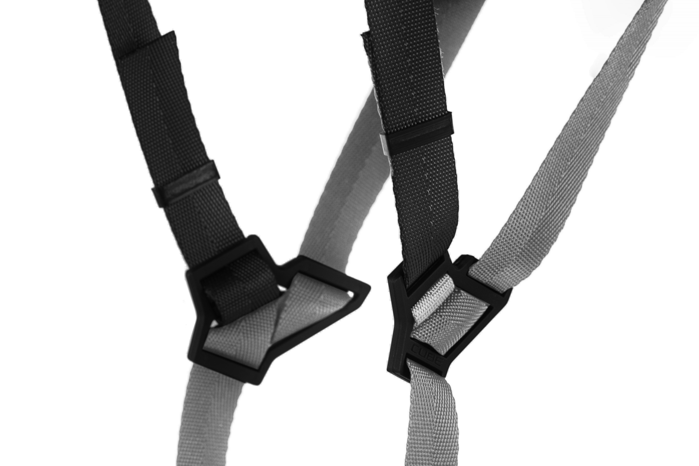 Nahaufnahme zweier ineinander verschlungener schwarzer und grauer Nylongurte mit dreieckigen Kunststoffschnallen des CUBE Helm ROAD RACE Rennradhelms von Cube, entwickelt für eine optimale Passform beim Rennradfahren, isoliert auf weißem Hintergrund.