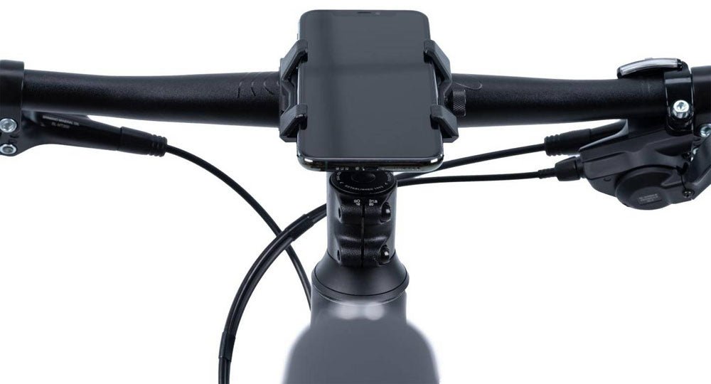 Bei der ACID Handyhalterung HPP von ACID sitzt ein Smartphone auf dem Lenker eines Fahrrads. Auf dem Foto, das aus der Sicht des Fahrers aufgenommen wurde, sind die Bedienelemente des Fahrrads und die Bremskabel zu sehen, wobei die Silikonpads das Telefon sicher halten.