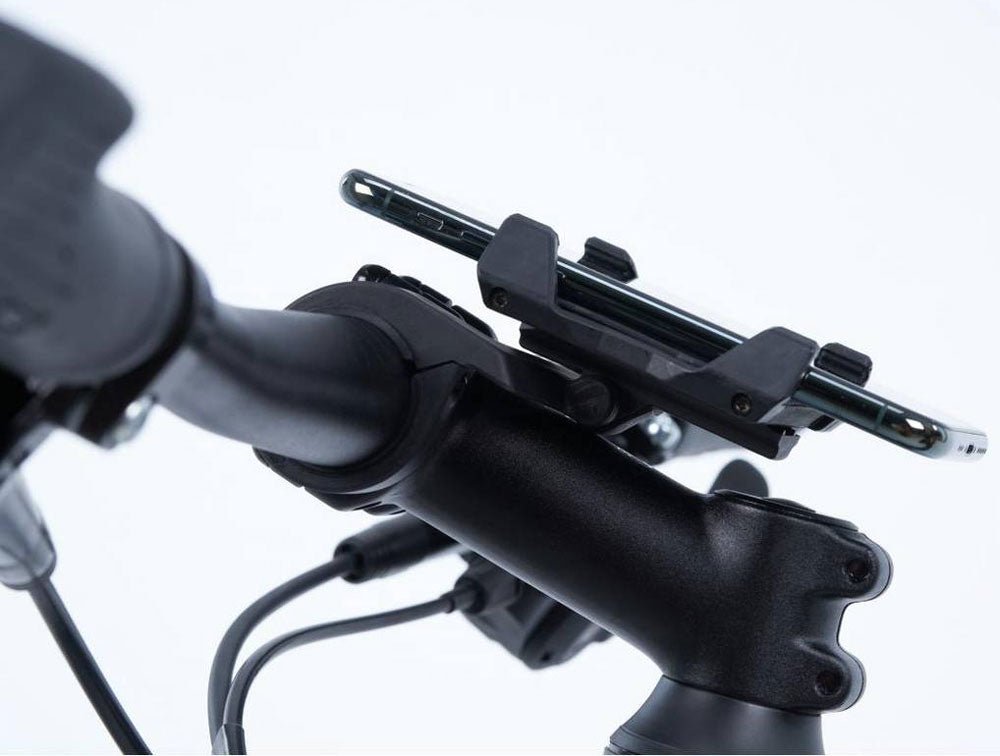 Nahaufnahme einer ACID Handyhalterung HPP von ACID, die an einem Fahrradlenker befestigt ist, mit sichtbaren Silikonpads neben einem Teil des Lenkers und Kabeln vor einem weißen Hintergrund.
