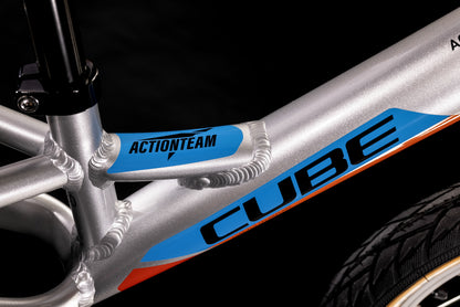 Nahaufnahme des Cube CUBE Cubie 120 walk actionteam Laufrad, ein leichtes Aluminium-Balancebike für Kinder, mit blauem ACTIONTEAM auf dem Oberrohr und CUBE Branding - ideal für junge Fahrer. Der schwarze Hintergrund hebt Teile des Sitzrohrs und des Reifens hervor.